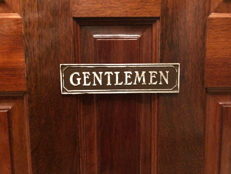 May include: A brown wooden door with a metal sign that reads "GENTLEMEN" in white lettering.