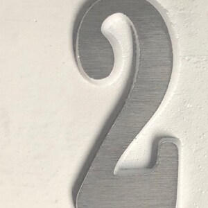 May include: A close-up of a silver number two, embossed on a white background.