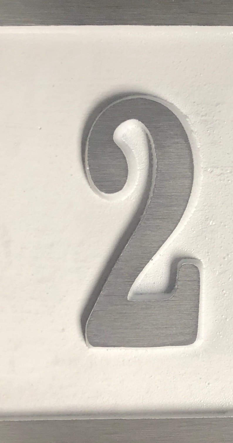 May include: A close-up of a silver number two, embossed on a white background.
