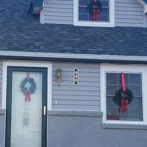 May include: A gray house with a black door and two windows. The door and windows are decorated with green wreaths and red bows. The house number 440 is displayed on the side of the house.