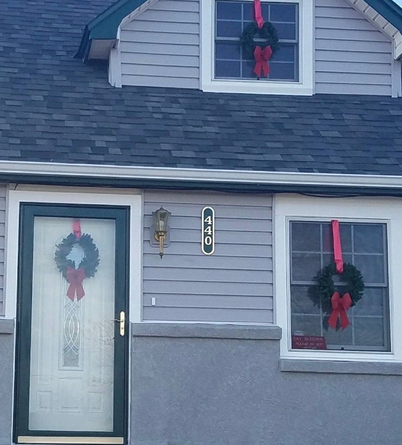 May include: A gray house with a black door and two windows. The door and windows are decorated with green wreaths and red bows. The house number 440 is displayed on the side of the house.