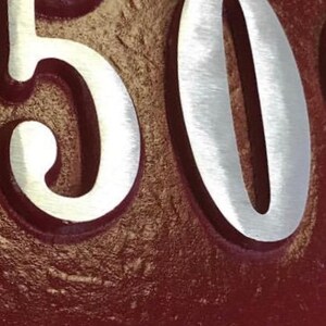 May include: A close-up of a house number plaque with the number "50" in silver lettering on a burgundy background.