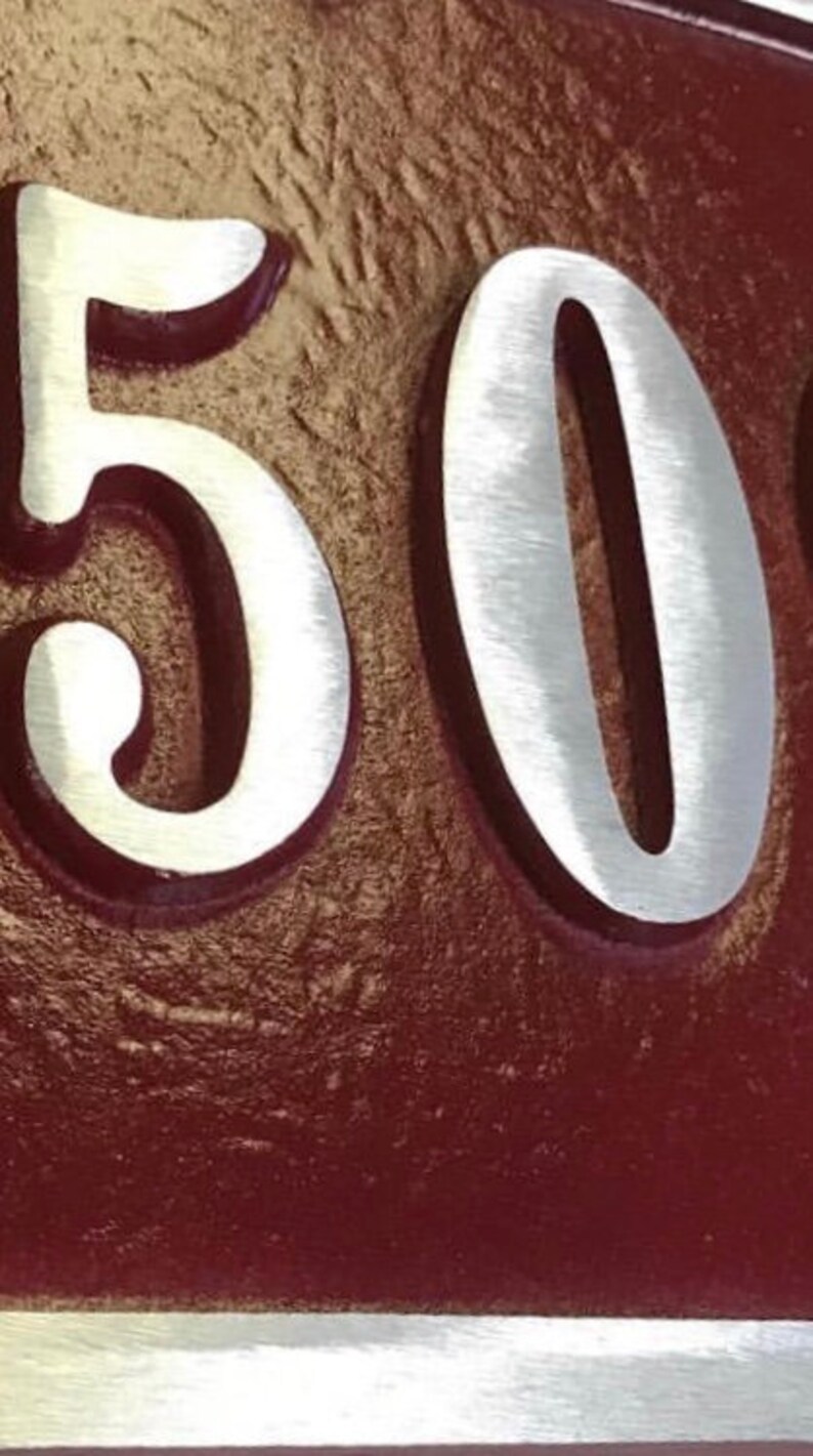May include: A close-up of a house number plaque with the number "50" in silver lettering on a burgundy background.