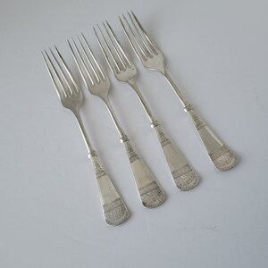 May include: Four silver forks with ornate handles. The forks are arranged in a row, with the handles pointing to the right. The forks are all the same size and shape.