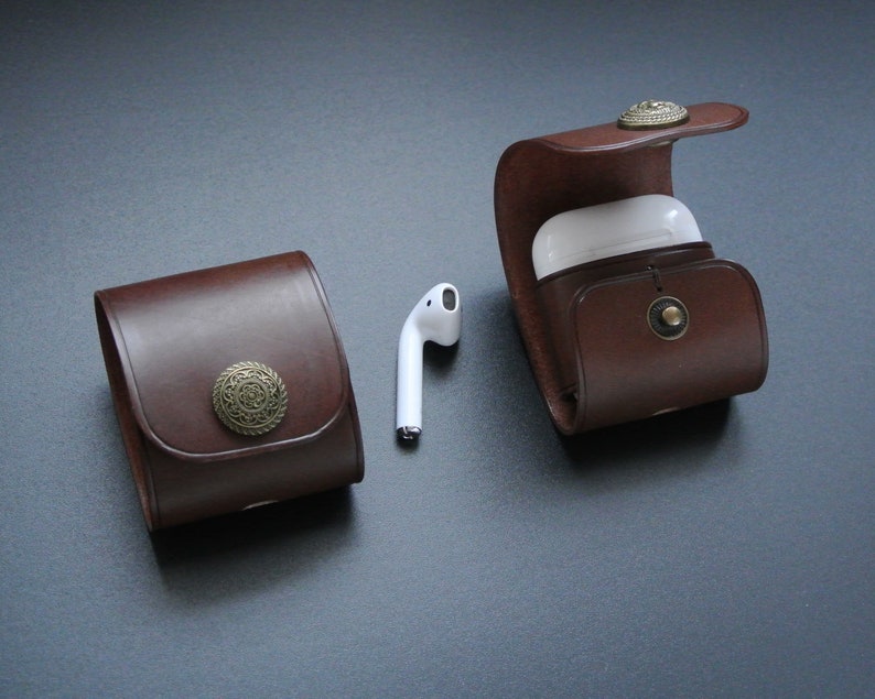 May include: Two brown leather cases with metal accents for holding wireless earbuds. One case is open and shows a white earbud case inside.