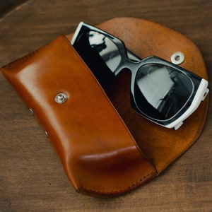 May include: A brown leather case with a black and white pair of sunglasses inside.