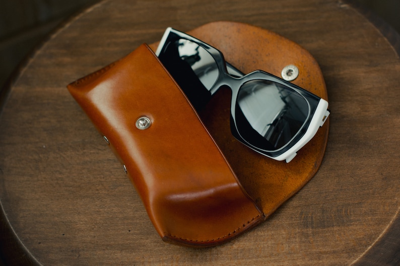 May include: A brown leather case with a black and white pair of sunglasses inside.