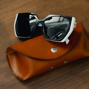 May include: Black and white sunglasses with a brown leather case. The sunglasses have a white frame with black lenses.