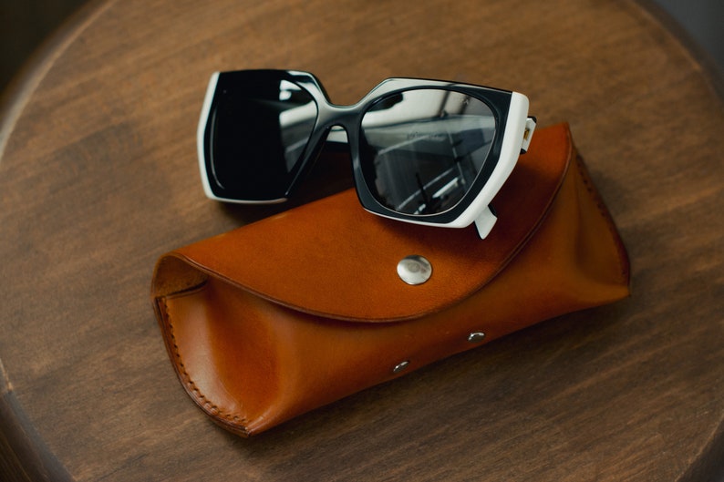 May include: Black and white sunglasses with a brown leather case. The sunglasses have a white frame with black lenses.