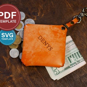 May include: An orange leather wallet with the name "DENYS" embossed on the front. The wallet is attached to a key ring and contains a stack of U.S. five-dollar bills. Several coins are scattered around the wallet.
