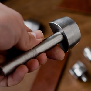 以下が含まれることがあります： 丸い頭とテクスチャ加工されたハンドルが付いた銀色の金属製の革パンチツールです。