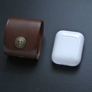 May include: A brown leather case with a lion head design and a white case for wireless earbuds.