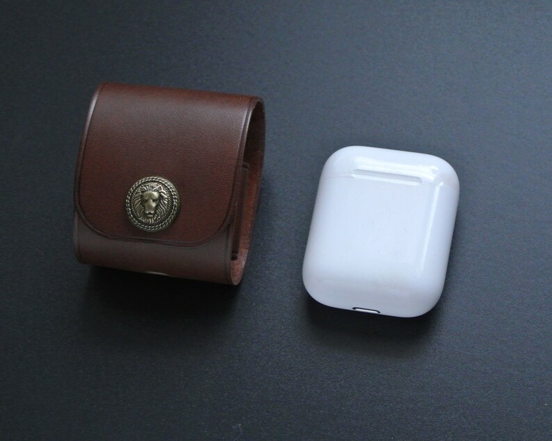 May include: A brown leather case with a lion head design and a white case for wireless earbuds.