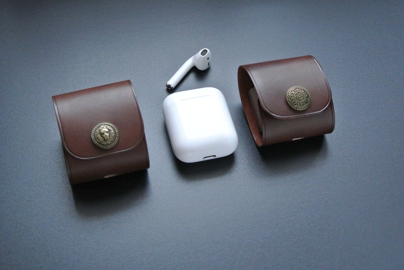 May include: Two brown leather cases with metal accents and a white wireless charging case for earbuds.