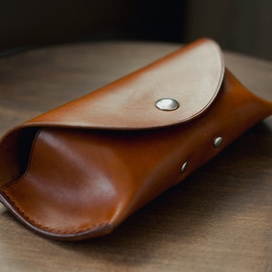 May include: A brown leather glasses case with a flap closure and silver snaps.