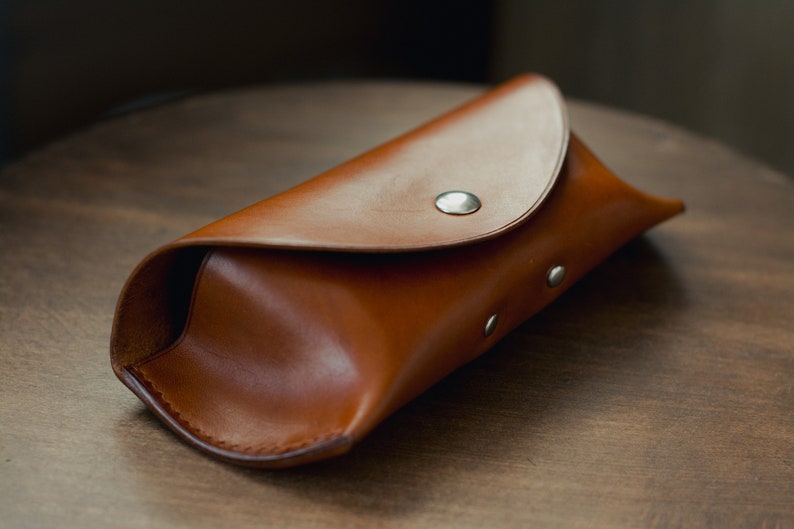 May include: A brown leather glasses case with a flap closure and silver snaps.