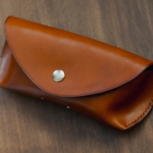May include: A brown leather glasses case with a silver button closure.