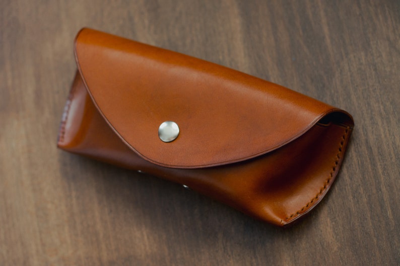 May include: A brown leather glasses case with a silver button closure.