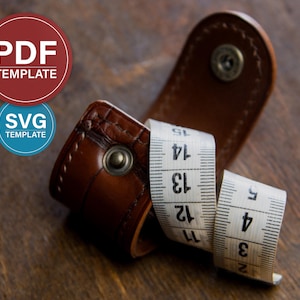 May include: A brown leatherette measuring tape case with a white measuring tape. The tape is marked with black numbers and lines. The case has a snap closure. The image also includes two circular graphics with the text "PDF TEMPLATE" and "SVG TEMPLATE".