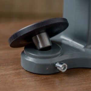 Puede incluir: Primer plano de una base de metal gris con un pie de goma negro y un tornillo plateado. La base tiene la palabra "TIEF" impresa en ella.