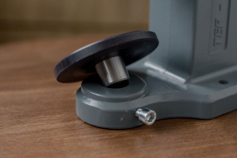 Puede incluir: Primer plano de una base de metal gris con un pie de goma negro y un tornillo plateado. La base tiene la palabra "TIEF" impresa en ella.