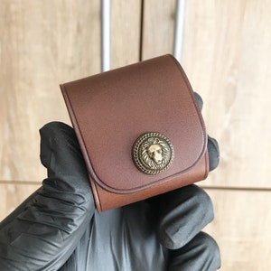 May include: A brown leather case with a lion head design on the front. The case has a brass clasp and is made of high-quality leather.