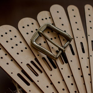 May include: A set of eight unfinished wooden belt straps with a brass buckle. The straps have rows of evenly spaced holes and a single slot for the buckle.