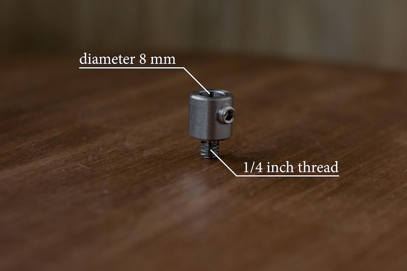 Puede incluir: Un conector de metal plateado con una rosca de 1/4 de pulgada y un di&aacute;metro de 8 mm. El conector est&aacute; sobre una superficie de madera.