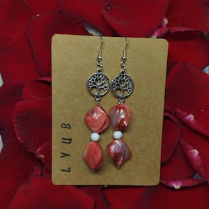 May include: A pair of silver earrings with a tree of life design and pink and white shell beads.