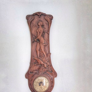 May include: A wooden barometer with an ornate carved design featuring a woman and a dog. The barometer face has a white background with black markings and the words "English  Barometer  Comp."