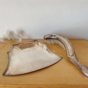 Peut inclure: Un ensemble de balayette et pelle à poussière en argent. La pelle à poussière a la forme d'un croissant de lune et possède une poignée. La brosse est incurvée et possède une brosse à poils blancs.