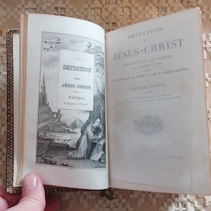 Puede incluir: Un libro antiguo titulado "Imitación de Jesucristo" con una ilustración en blanco y negro de un hombre arrodillado en oración. El libro tiene una encuadernación dorada.
