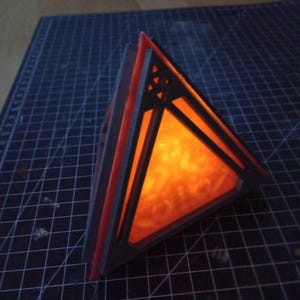 May include: A black and orange geometric lamp with a triangular shape and a glowing orange light inside.