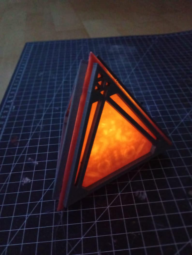 May include: A black and orange geometric lamp with a triangular shape and a glowing orange light inside.