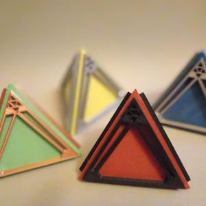 May include: Four geometric pyramid-shaped objects with different coloured surfaces. The pyramids are made of a layered material with a black outline. The colours are green, red, yellow, and blue.