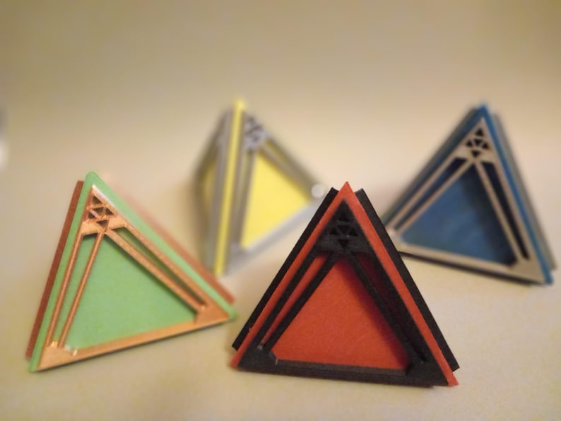 May include: Four geometric pyramid-shaped objects with different coloured surfaces. The pyramids are made of a layered material with a black outline. The colours are green, red, yellow, and blue.