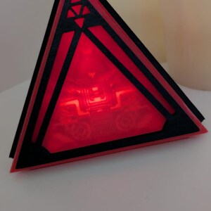 May include: A red triangular prism with black geometric designs and a glowing red light inside.