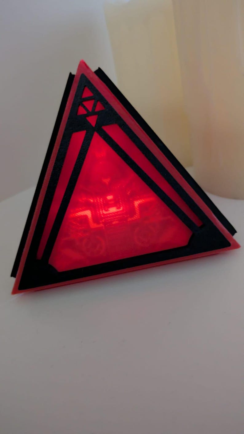 May include: A red triangular prism with black geometric designs and a glowing red light inside.