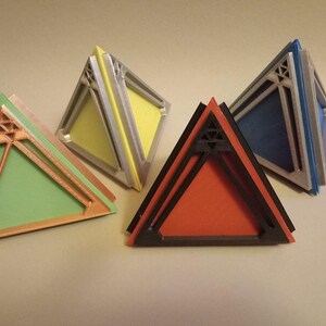 May include: Four triangular shaped boxes made of layered cardboard. The boxes are in different colours: green, yellow, red, and blue. Each box has a decorative design on the front.