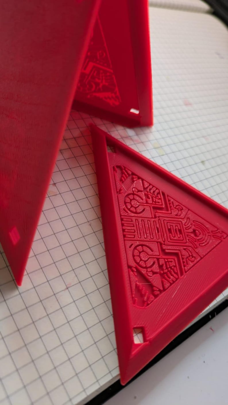 May include: Three red plastic triangular shapes with intricate designs on the surface. The shapes are arranged in a pyramid formation.