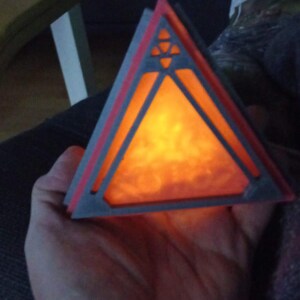 May include: A triangular, 3D printed lamp with a geometric design. The lamp is lit and glows orange.