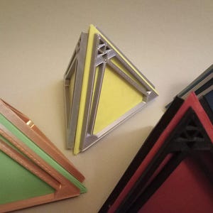 May include: Four geometric pyramid-shaped boxes with intricate designs. The boxes are made of different materials and colours, including silver, yellow, red, and black.