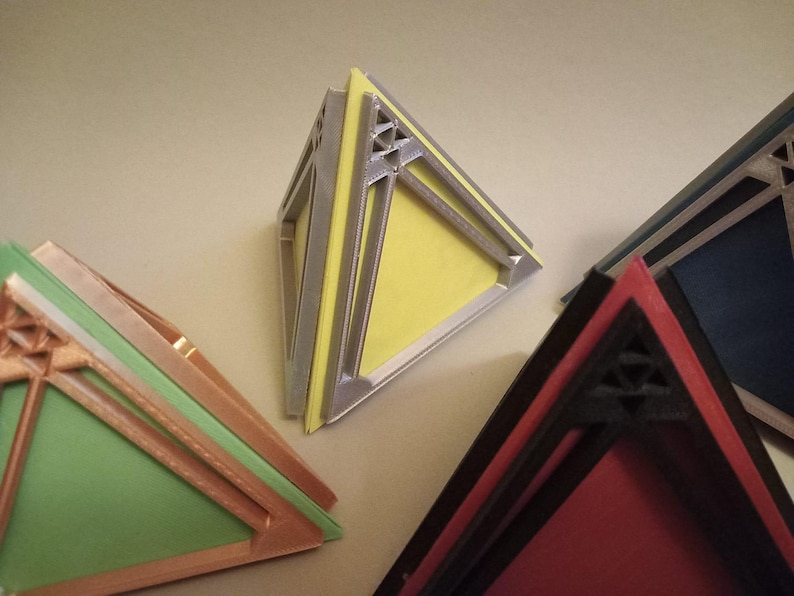 May include: Four geometric pyramid-shaped boxes with intricate designs. The boxes are made of different materials and colours, including silver, yellow, red, and black.