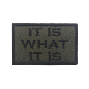 Peut inclure: Un patch brod&eacute; vert avec des coutures noires qui dit "IT IS WHAT IT IS".