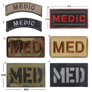 Puede incluir: Diez parches bordados diferentes con la palabra "MED" o "MEDIC" en varios colores y estilos. Los parches miden aproximadamente 4 cm por 8 cm.