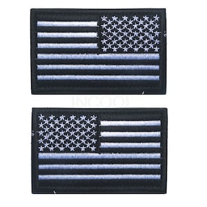 Pu&ograve; includere: Due toppe ricamate con la bandiera americana in bianco e nero. Le bandiere sono bianche su nero con un contorno bianco attorno alle stelle e alle strisce.