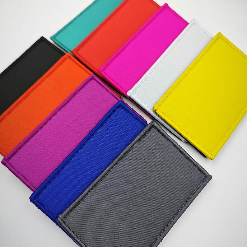 May include: Assortment of fabric patches in various colours, including black, orange, pink, blue, grey, white, yellow, red, and teal. The patches are rectangular and have a stitched border.