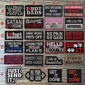 Può includere: Una collezione di toppe ricamate nere e colorate con varie frasi e disegni. Le toppe includono testo come "Allergico alle persone stupide", "I Hot Dads" e "Game Over". Alcune toppe hanno una forma rettangolare, altre sono più stilizzate.