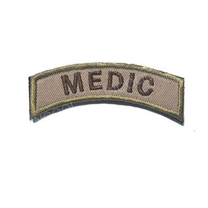 May include: A tan curved patch with a green border and the word "MEDIC" embroidered in brown.