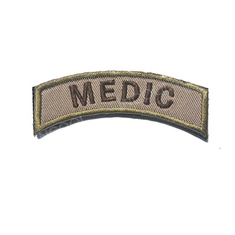 May include: A tan curved patch with a green border and the word "MEDIC" embroidered in brown.